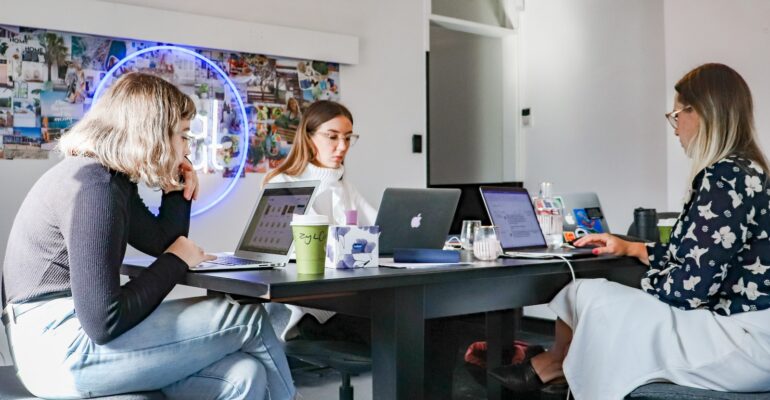 3 women sitting on chair in front of table with laptop computers