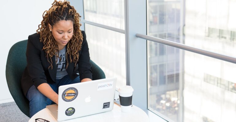 woman sits on padded chair while using MacBook during daytime